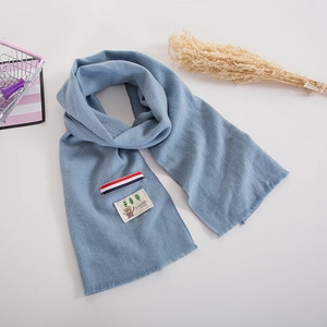 Close-up of soft light blue knit scarf featuring a cute cartoon bear patch and striped detail