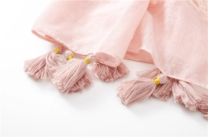 Detail of light pink summer scarf featuring lace stitching and golden thread tassels