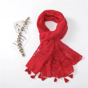 Detail of red scarf with floral lace patchwork and decorative tassels on white backdrop
