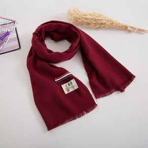 Detail of soft burgundy knit scarf with cute bear patch, tricolor ribbon and short tassels
