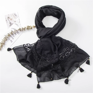 Close-up of black scarf featuring delicate lace patchwork and tassel with gold rings