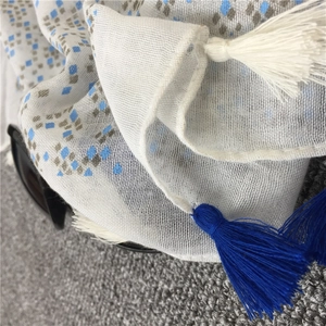Dettaglio di sciarpa in cotone e lino bianco con motivi a rombi blu e frange