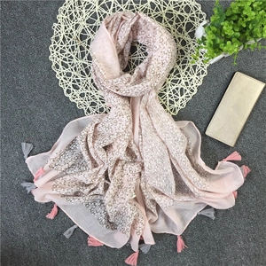 Dettaglio di sciarpa in cotone rosa con pois metallici argento e bordi con frange su stuoia
