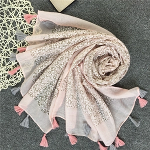 Dettaglio di sciarpa rosa chiaro con stampe geometriche argento e nappe bicolore