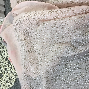 Dettaglio di sciarpa leggera rosa con motivi geometrici grigi e bianchi e frange