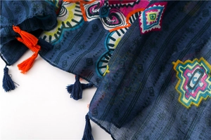 Détail d'une écharpe bohème bleu foncé avec motifs géométriques et pompons bicolores