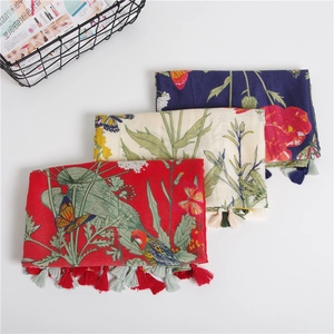 Detailed view of floral and bird print scarves with fringe in red, cream, and navy blue