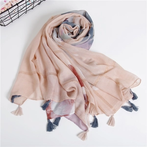 Détail d'une écharpe en coton rose clair avec motifs quadrillés dorés et pompons colorés