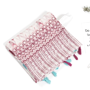 Detail of red-brown geometric printed scarf with colorful tassels and soft linen texture
