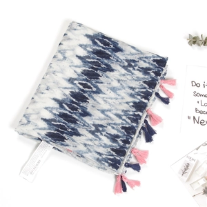 Detail of blue ikat print scarf showing vibrant pink and navy tassels with care label
