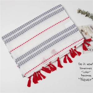 White linen scarf with geometric red and blue patterns and decorative red fringe tassels