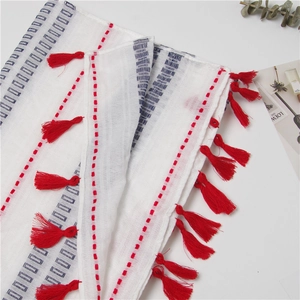 Detail view of a white linen scarf featuring red tassel edges and blue geometric patterns