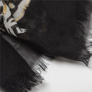Detailed macro view of black scarf featuring gold paisley print and fringe edges