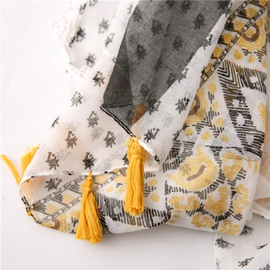 Detail of cotton linen scarf featuring white lace edges and bright yellow tassels
