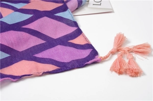 Détail d'une écharpe à motifs géométriques avec un pompon rose sur un tissu multicolore