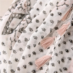 Macro detail of breathable white cotton scarf with black geometric prints and pink tassels