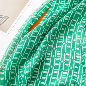 Détail de l'écharpe verte avec motifs géométriques blancs et doublure orange vif