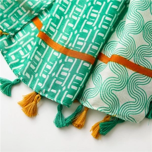 Détail d'une écharpe bohème avec motifs à vagues verts, bords orange et glands colorés