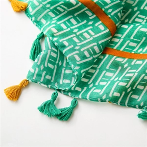 Gros plan d'une écharpe verte en coton avec motifs géométriques et pompons colorés