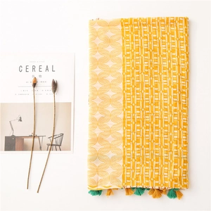 Détail d'une écharpe imprimée jaune avec motifs géométriques blancs et bords à franges