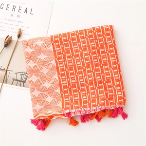 Détail d'une écharpe en coton et lin avec motifs géométriques et pompons orange