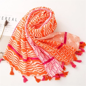 Détail d'une écharpe en lin bicolore orange et rose avec pompons et motifs variés