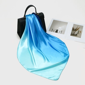 Dettaglio di un foulard in raso blu sfumato drappeggiato su una borsa in pelle nera