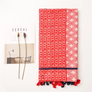Mise à plat d'une écharpe en coton rouge à motifs géométriques et pompons sur blanc