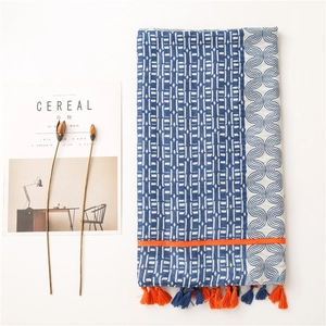 Détail d'une écharpe en coton et lin bleu et blanc avec des pompons orange vif