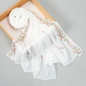Detail of white chiffon scarf with pink floral embroidery and lace edges on wooden tray