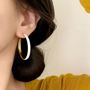 Elegant gold-trimmed white enamel C-shaped hoop earrings on a model with minimalist style