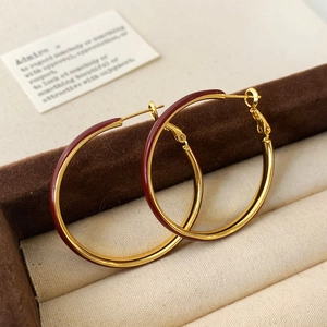 Close-up of elegant gold hoops with burgundy enamel finish in a premium jewelry box