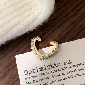 Detail of a golden heart ear cuff with micro-pave zircons on a warm aesthetic background