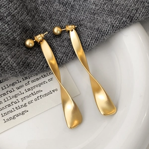 Detail view of long twisted matte gold earrings on a minimalist textured surface