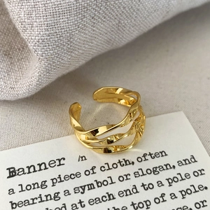 Detail of a gold layered twisted geometric open ring with polished metal texture