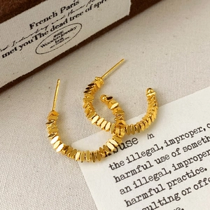 Detailed close-up of C-shaped gold-plated hoop earrings with textured grain design