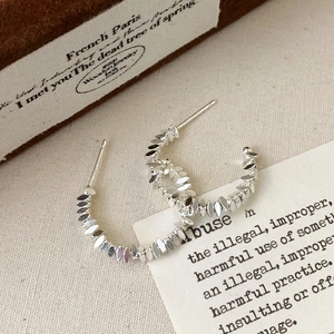 Macro shot of silver olive leaf C-shaped earrings on vintage paper and linen background
