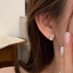 Elegante Goldohrringe mit rechteckigem Zirkon und weißer Perle am Ohr des Modells