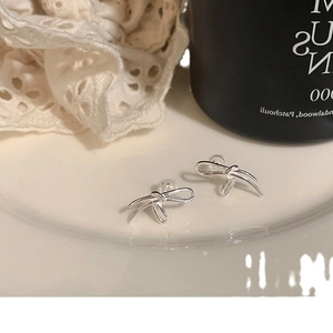 Minimalist silver bow knot earrings for women shown on a white ceramic plate decoration