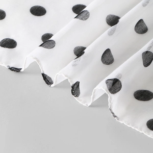 Detail of white voile fabric with black polka dots showing mesh texture and soft draping