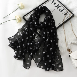 Detail of soft black voile scarf with white polka dots draped on a plush white texture
