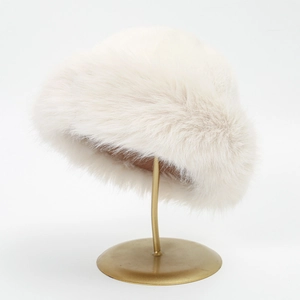 Close-up of white plush Mongolian style faux fur hat with thick warm texture on gold stand
