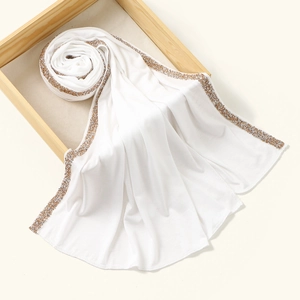 Detailed view of white chiffon turban with elegant gold sequin borders on wooden tray