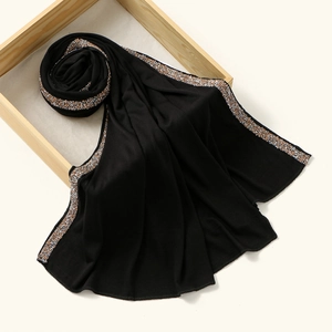 Detailed close-up of soft black jersey scarf featuring shimmering rhinestone trim on wooden tray