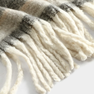 Close-up detail of soft winter plaid scarf with fringe texture, cozy cashmere feel.