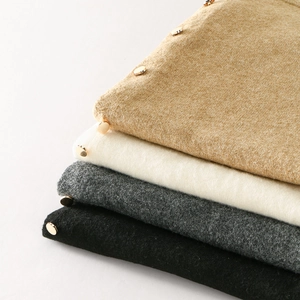 Detail of stacked knitted shawls in four colors with decorative golden metal buttons