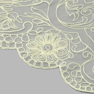 Macro shot of light yellow floral lace embroidery on fine mesh fabric with wavy edges