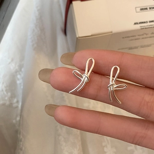 Detail shot of silver bow stud earrings with delicate line knot design on lace background