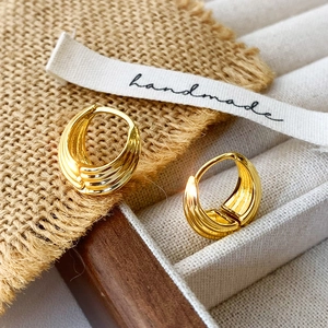 Close-up of golden triple-layered textured hoop earrings on a vintage fabric background