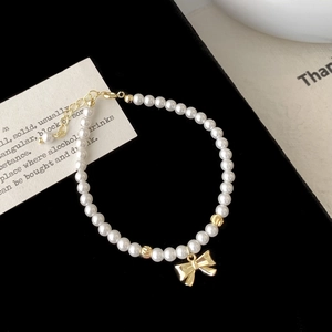 Détail du bracelet en perles blanches avec pendentif nœud doré et chaîne ajustable